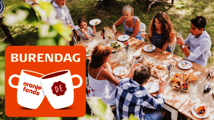 Grote tafel met lunch buiten in het groen met veel verschillende mensen. Met logo Burendag.