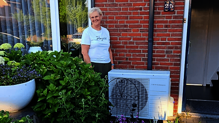 Anne-Marie in haar voortuin naast de buitenunit van de hybride warmtepomp