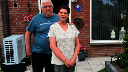 Eri en Gerard in de voortuin van hun woning met op de achtergrond de buitenunit van de hybride warmtepomp naast hun voordeur.